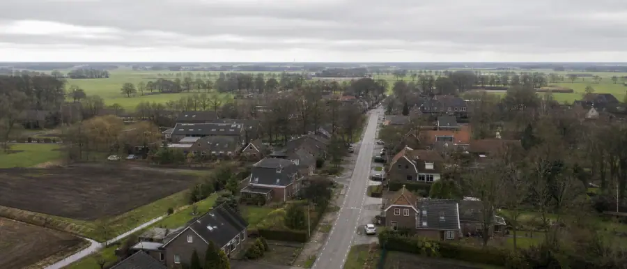 Uitzicht over een Drents lintdorp met bakstenen woningen langs een rechte weg en akkers erachter